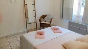 A hotel room with a bed, two towels, a chair, a ladder, and a window. - Joli appartement avec jardinet (Hyères)