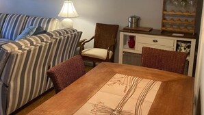 A cozy living room with a striped sofa, a wooden dining table with a decorative placemat, a wicker chair, a lamp, and a cabinet with glassware. - 5 block walk to the boardwalk at  Stockley (Rehoboth Beach)