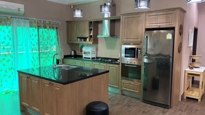 A modern kitchen with wooden cabinets, stainless steel appliances, a central island, and a small wooden table. - Big Comfortable Villa (Banglamung)