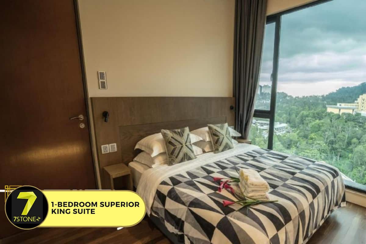 Eine Superior-Königssuite mit einem Schlafzimmer, einem Kingsize-Bett, einem Nachttisch, einem Holzschrank und Blick auf eine bewaldete Landschaft durch ein großes Fenster.