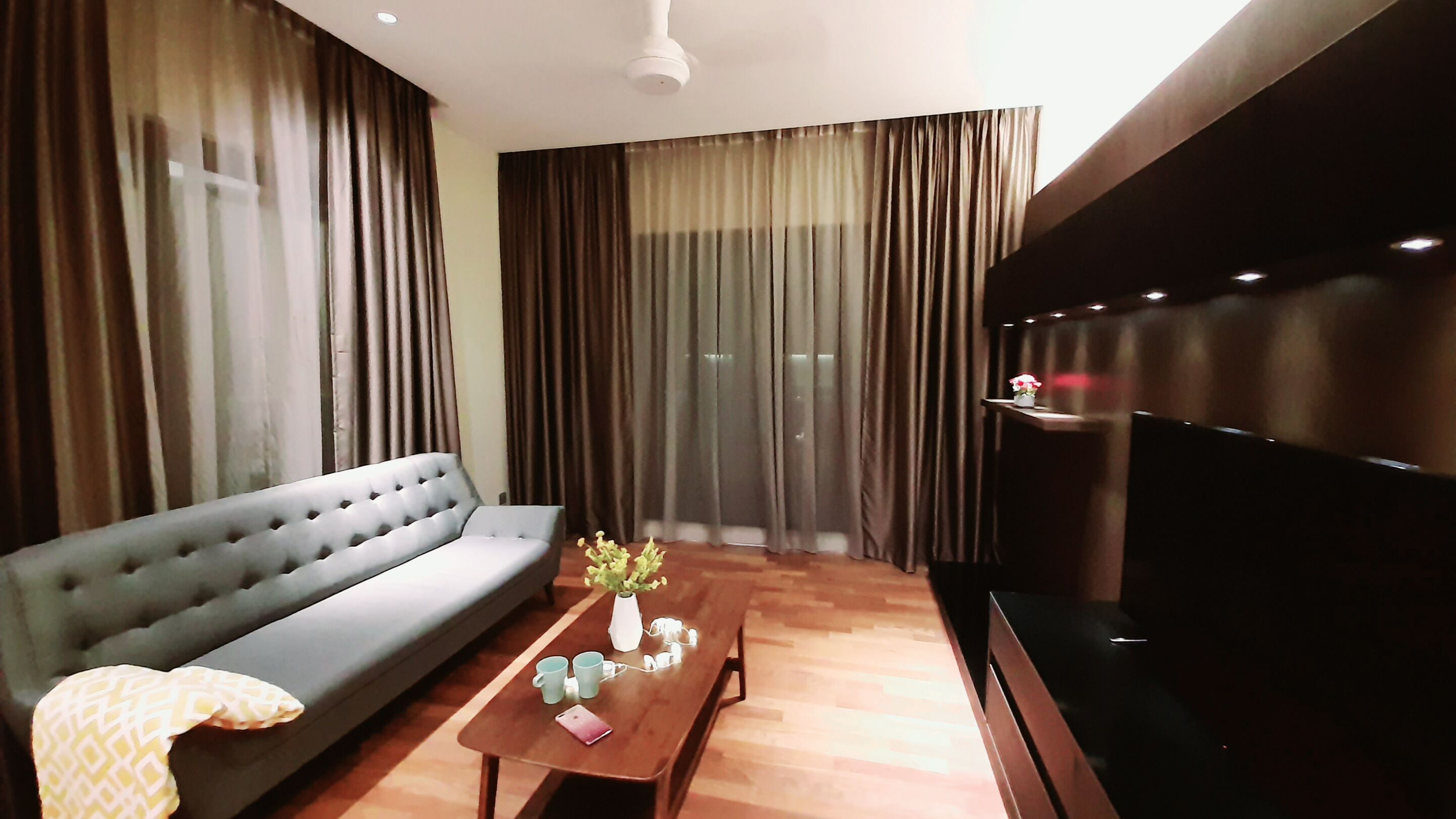 A living room with a sofa, a coffee table with a vase and cups, and a TV on a stand.