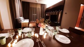 A dining area with a table set for a meal, including plates, glasses, and cutlery. There is a sofa and a TV in the background.