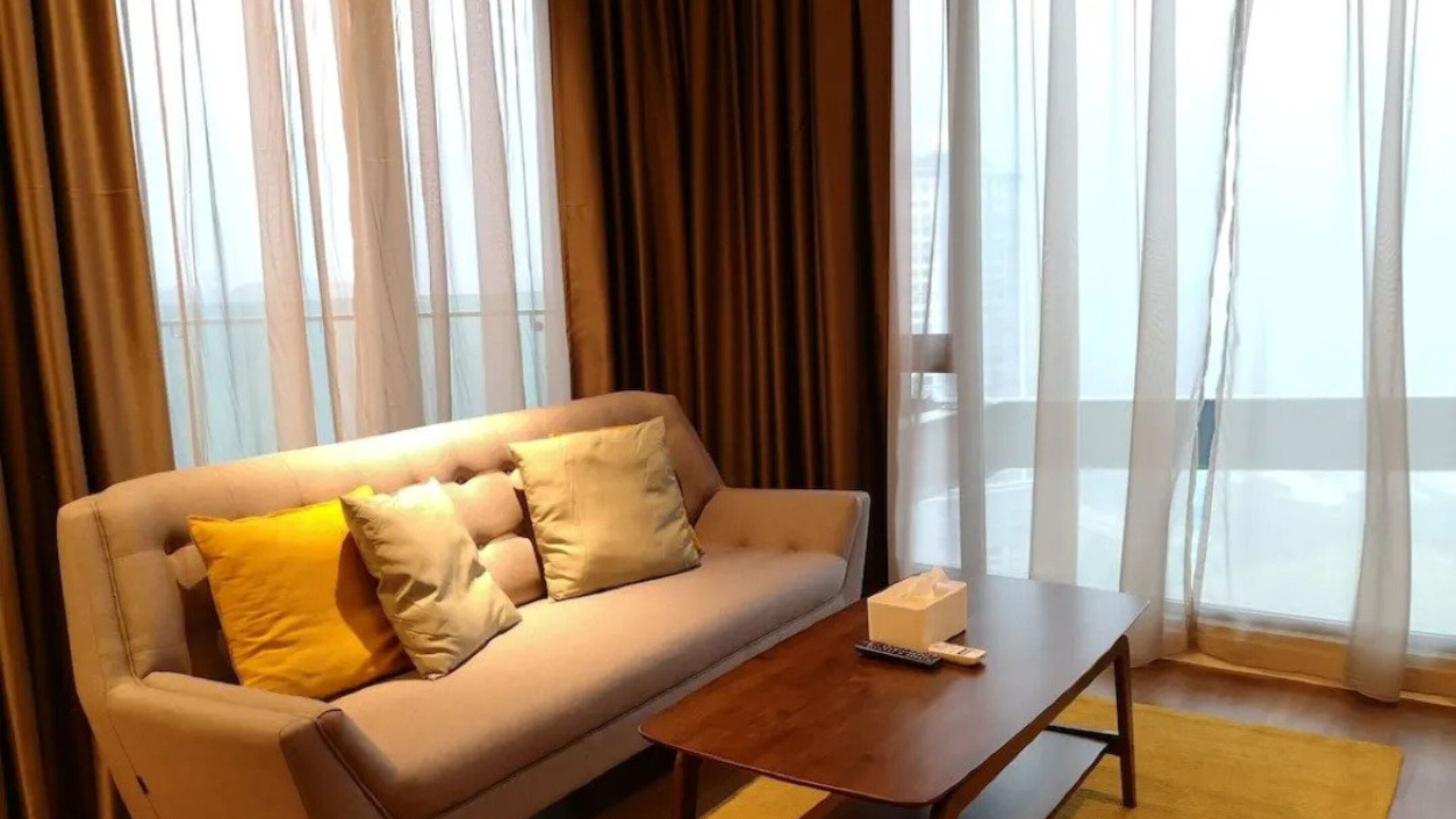 A hotel room with a sofa, a coffee table, and a window with curtains.