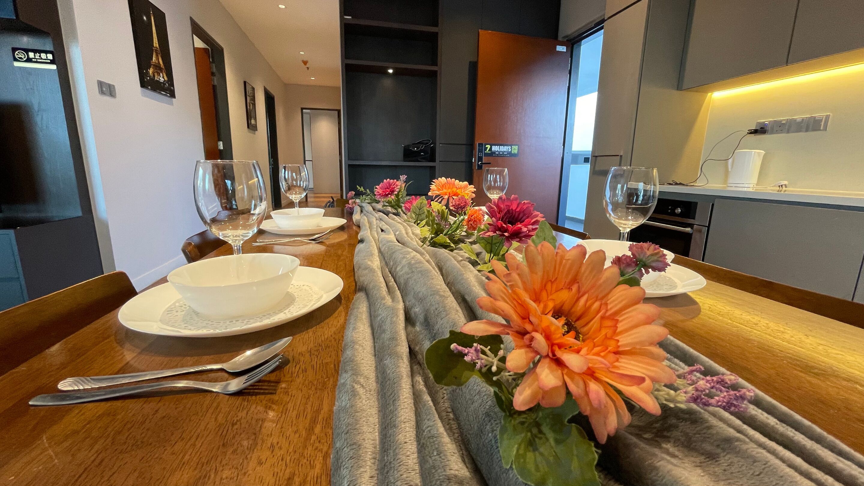 A dining area with a long table set for two, featuring white plates, bowls, and cutlery.
