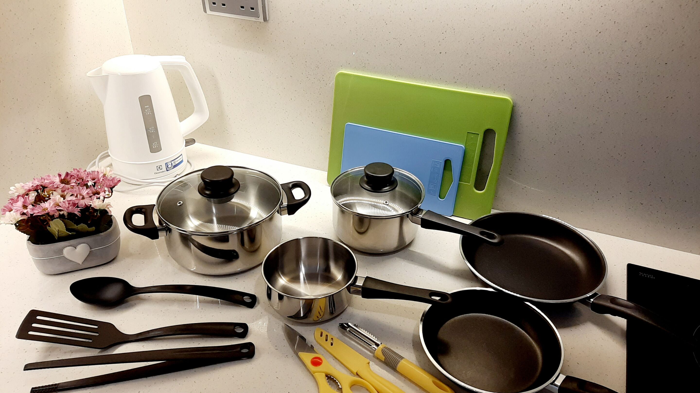 A kitchen counter with various cooking utensils, pots, a kettle, and a cutting board.