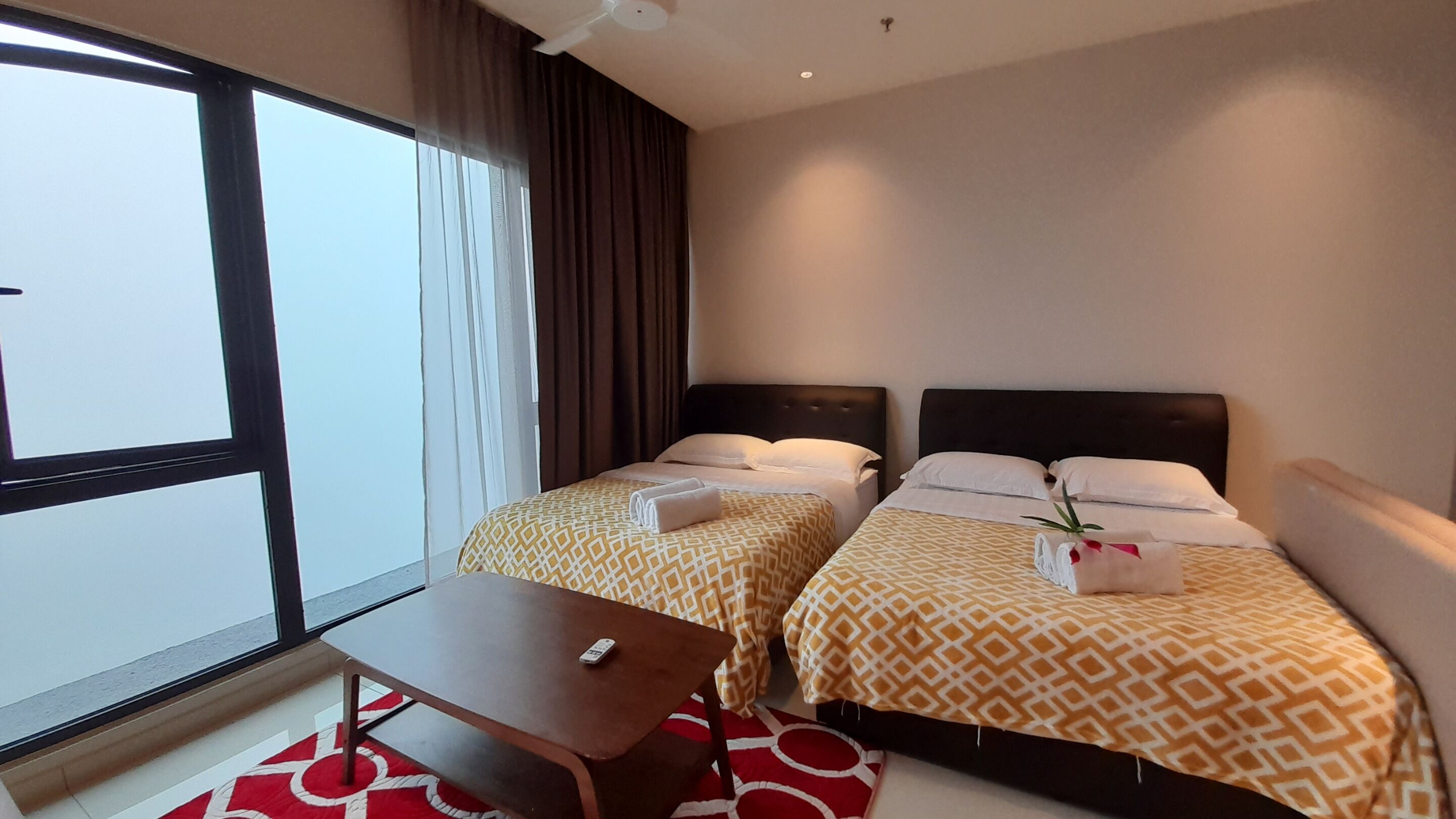 A hotel room with two beds, a small table, and a window with curtains.