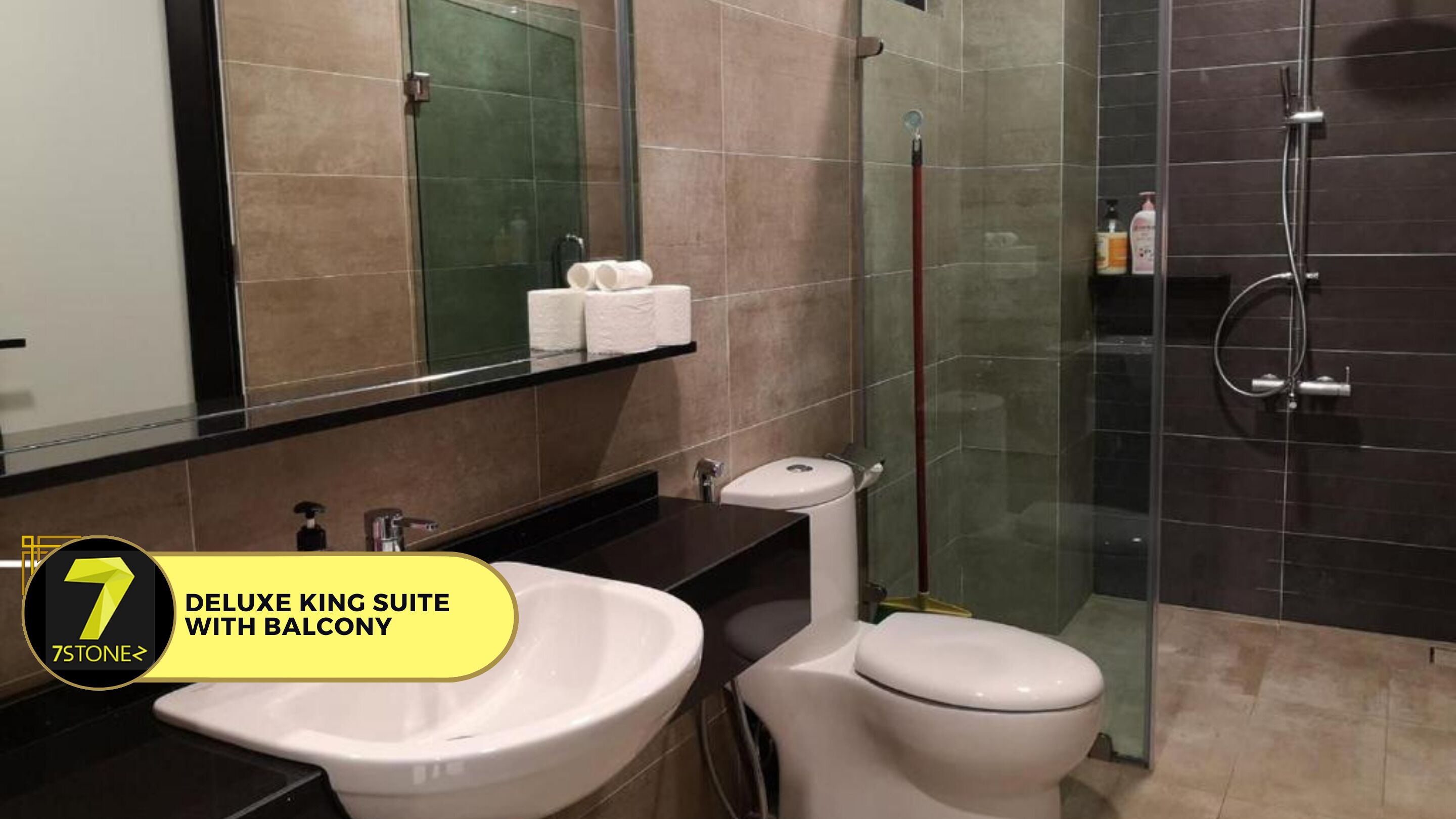 A bathroom with a sink, toilet, and shower. There is a mirror above the sink and a towel rack with towels. The walls are tiled, and there is a glass shower enclosure.