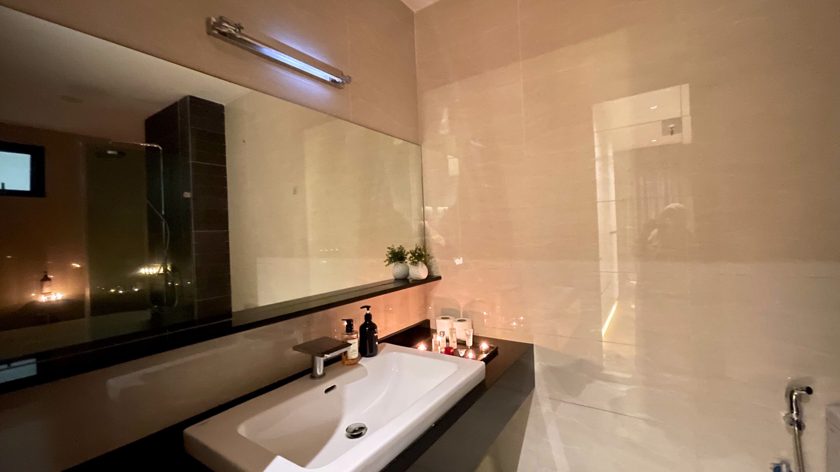 A modern bathroom with a large mirror, a sink, and a shower.