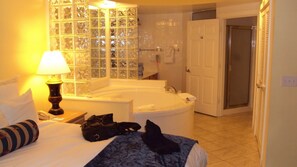 Ein Hotelzimmer mit einem großen Bett, einer Sitzecke mit Blick auf eine Glaswand, einer Badewanne und einer Tür zu einem weiteren Raum.