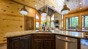 A spacious kitchen with wooden walls, a granite countertop, and a stainless steel dishwasher. - Jolly Roger Cabin | Pirate Ship Playground | Luxury Broken Bow Retreat (BROKEN BOW)