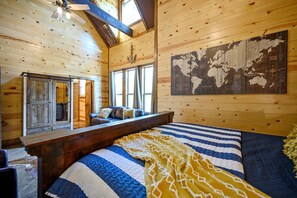 A wooden cabin interior with a bed, a map on the wall, and a window overlooking the outside. - Jolly Roger Cabin | Pirate Ship Playground | Luxury Broken Bow Retreat (BROKEN BOW)