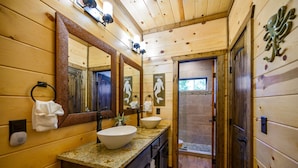Une salle de bain rustique, avec des murs en bois, un grand miroir, deux lavabos et un espace douche.