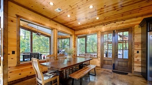 L’intérieur d’un chalet en bois comprend une grande table à manger, des bancs et de grandes fenêtres qui offrent une vue sur la forêt environnante.