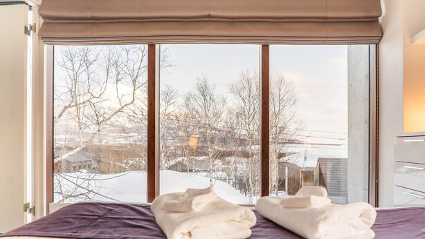 A hotel room with a large window, a bed with a purple bedspread, and two folded white towels on the bed. - Yuuki Toride Chalet (Kutchan)