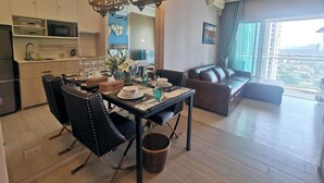 A modern living room with a dining area, a ceiling fan, and a large window with a city view. - 456 Veranda Residence Pattaya Jomtien Sea View 1BR; Beachfront (Chonburi)