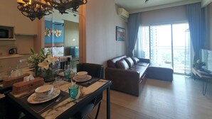 A modern living room with a brown leather sofa, a dining table set with plates, glasses, and a vase of flowers. A chandelier hangs from the ceiling, and a ceiling fan is visible. - 456 Veranda Residence Pattaya Jomtien Sea View 1BR; Beachfront (Chonburi)