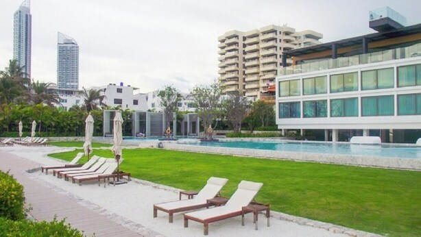 A hotel with a swimming pool, lounge chairs, and modern buildings in the background. - 456 Veranda Residence Pattaya Jomtien Sea View 1BR; Beachfront (Chonburi)
