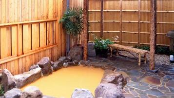Una cerca de madera, una piscina de piedra y un banco de madera en un patio.