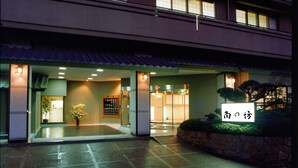 L’entrée d’un hôtel, avec une enseigne japonaise traditionnelle, un comptoir d’accueil et un espace d’attente agrémenté d’une plante en pot.