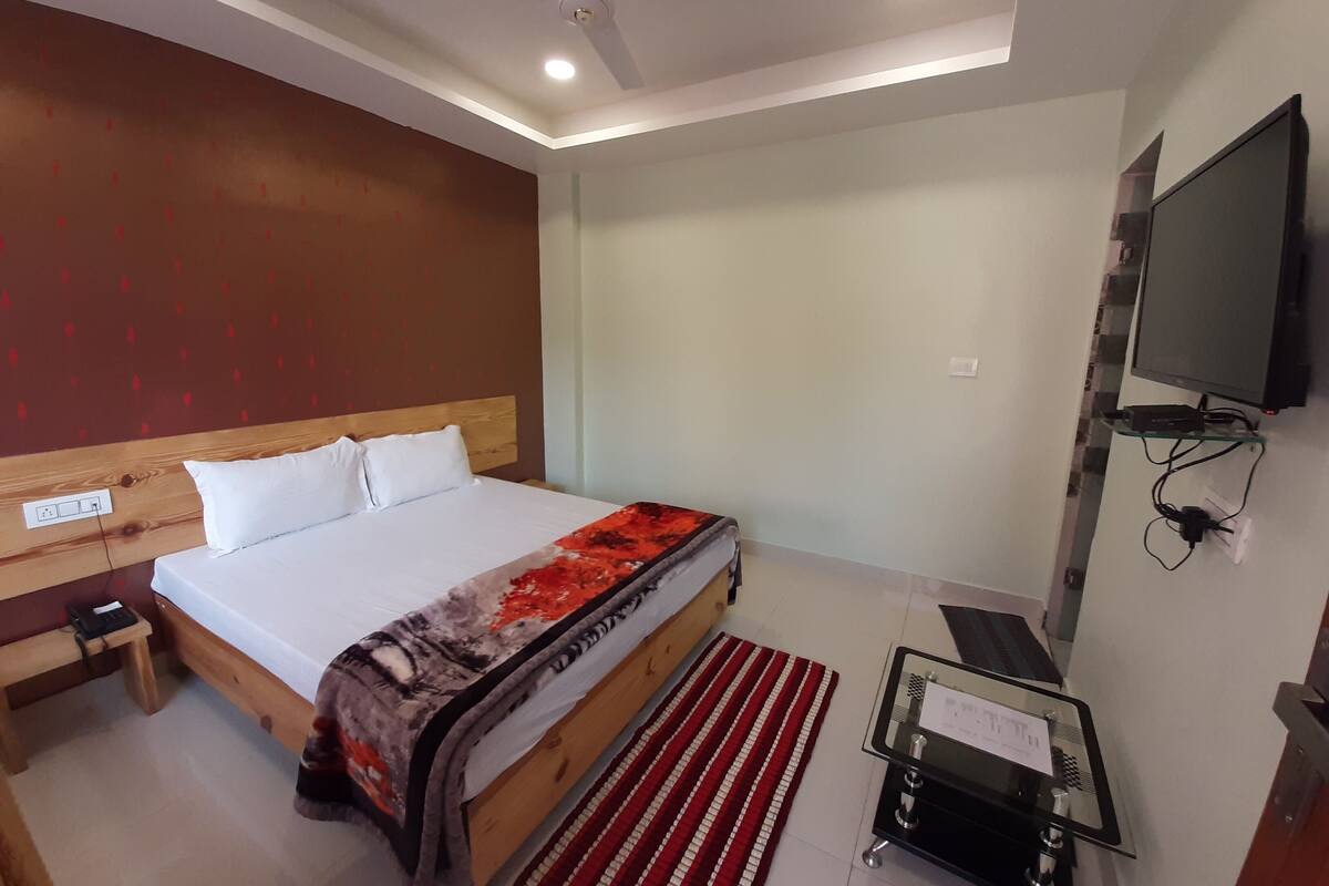 A hotel room with a bed, bedside table, TV, and a small desk with a chair.