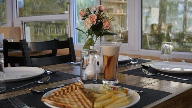 Ein Esstisch mit einer Speisenplatte, einem Glas Eistee und einer Blumenvase.