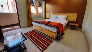 Ein Schlafzimmer mit einem hölzernen Bett, einem Glastisch, einem Streifen Teppich und Blick ins Freie durch ein Fenster.