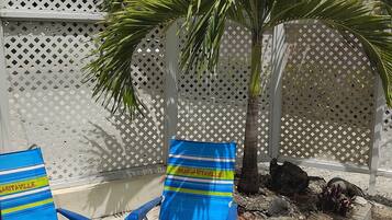 Eine Terrasse mit zwei Liegestühlen, einer Palme und einem Zierzaun.