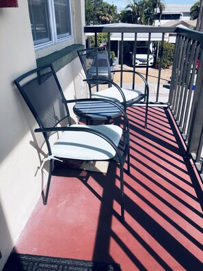 A balcony with two chairs and a table, a red floor, and a white wall.