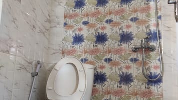 A bathroom with a toilet, a shower, and a tiled wall with a floral pattern.