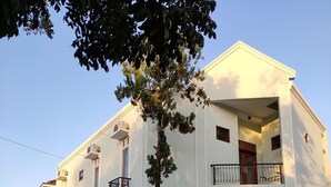 A two-story building with a white facade, a balcony with a black railing, and a garage door. - ZG Homestay Solo (Surakarta)
