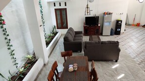 A living room with a sofa, a TV, and a dining table with chairs. There is a small garden area with plants and a window with curtains. - ZG Homestay Solo (Surakarta)