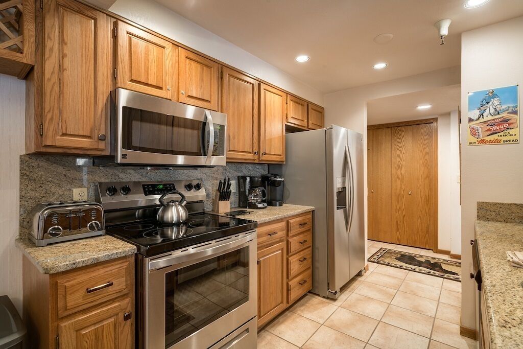 Una cocina con armarios de madera, electrodomésticos de acero inoxidable, encimeras de granito y piso de baldosas.