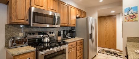 Una cocina con armarios de madera, electrodomésticos de acero inoxidable, encimeras de granito y piso de baldosas.