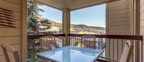 Un balcone con tavolo e sedie in vetro, che offre vista su un paesaggio innevato e edifici in lontananza.
