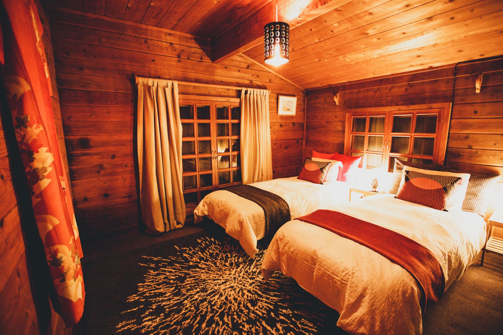 A cozy cabin-style bedroom with two beds, wooden walls, and a large window.