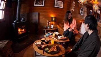 A cozy room with a wood-burning stove, wooden walls, and a dining table with food and drinks.