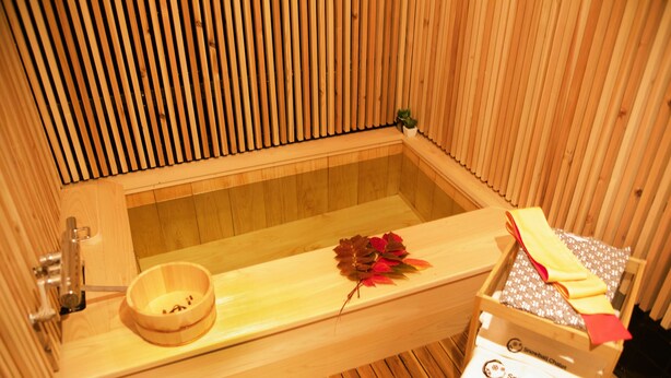 Un sauna en bois avec un banc, un petit récipient en bois et une boîte à serviettes portant l’inscription « Chalet Snowball ».
