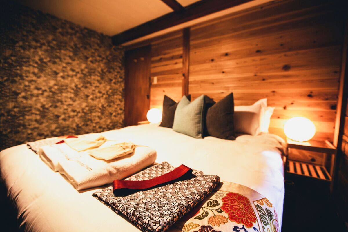 Un lit bien fait, avec des oreillers et des serviettes pliées, une tête de lit en bois et une table de chevet avec une lampe.