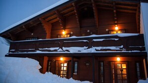 Un chalet en bois, dont le toit est recouvert de neige et qui possède de nombreuses fenêtres illuminées.