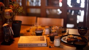 Une table dressée avec un livre intitulé « WABI-SABI, BIENVENUE », divers plats et une petite statue.