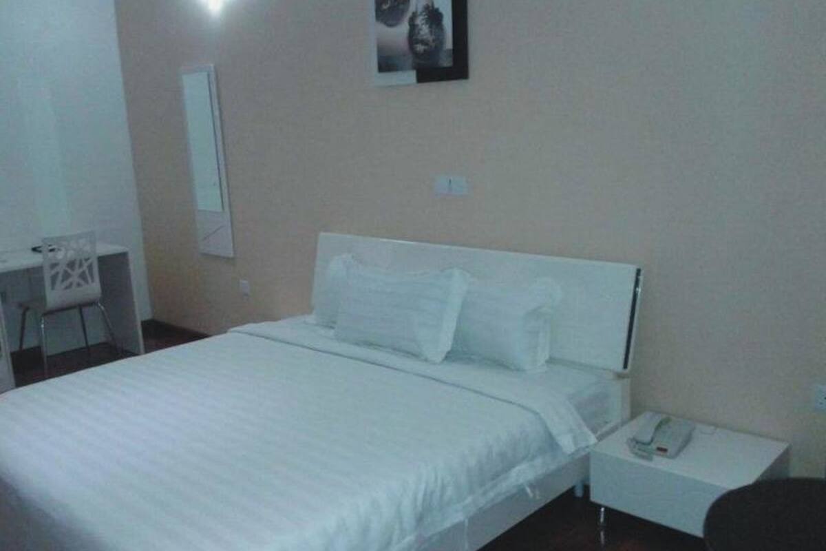 A bedroom with a bed, a nightstand with a phone, a desk with a chair, and a wall-mounted picture.