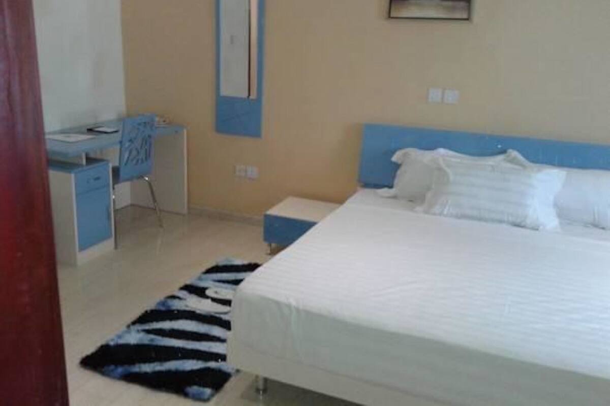 A bedroom with a bed, a desk, a chair, and a mirror.