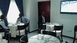 A conference room with round tables, chairs, and a television screen. - Newcastle Hotel (Lagos)