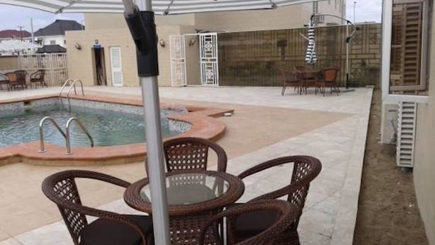 An outdoor pool area with a covered seating area and a poolside chair. - Newcastle Hotel (Lagos)