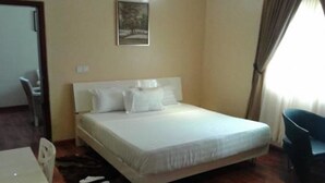 A neatly arranged bedroom with a bed, a chair, and a desk. - Newcastle Hotel (Lagos)