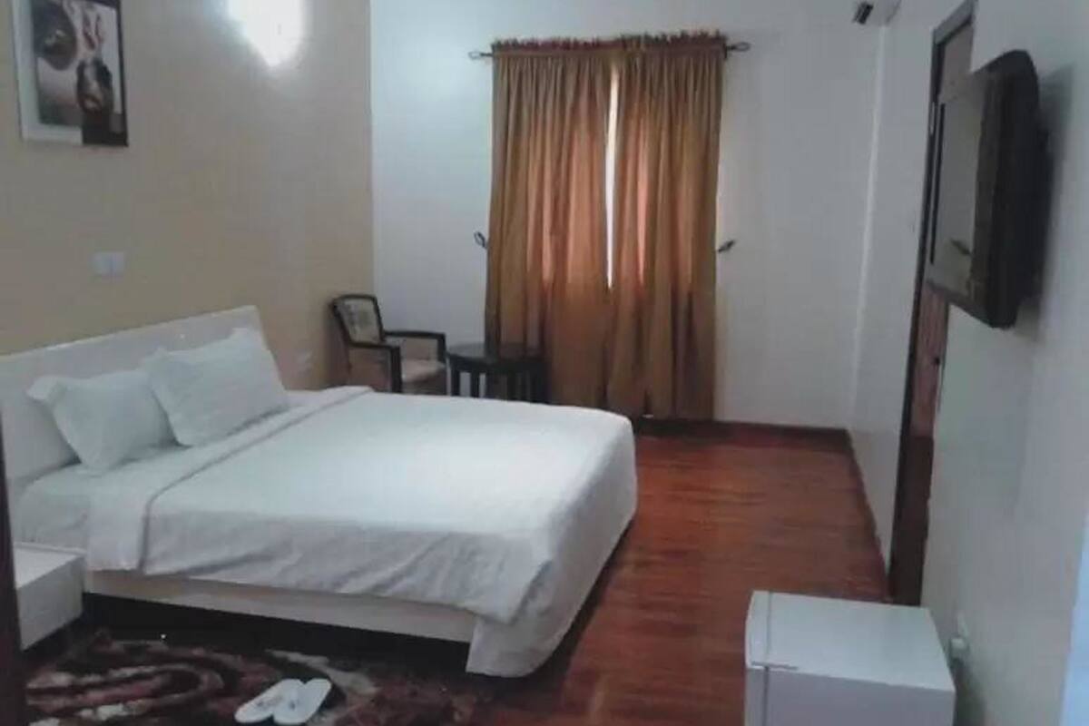 A bedroom with a bed, a small table, a chair, a television, and a window with curtains.