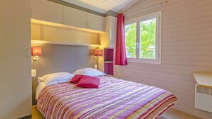 Una camera da letto con un letto, due lampade ai comodini, una finestra con tende e una libreria a muro.