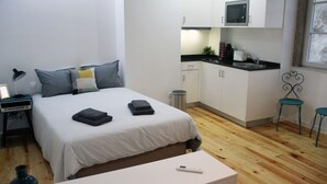 A bedroom with a bed, bedside table, lamp, and a small table with a remote control.