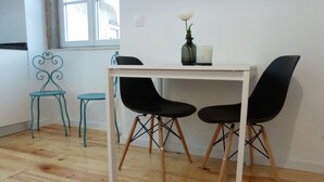 A dining area with a white table and four black chairs, a teal chair, and a vase with a flower on the table.