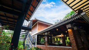 A traditional building with a brick facade, a balcony, and a covered outdoor seating area with hanging plants. - Mount Xanadu (Sulthan Bathery)